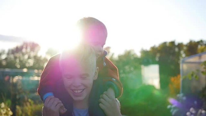 男孩拥抱他的弟弟，把他抱在肩上。孩子们的欢笑和喜悦。日落