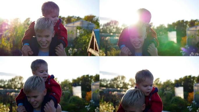 男孩拥抱他的弟弟，把他抱在肩上。孩子们的欢笑和喜悦。日落