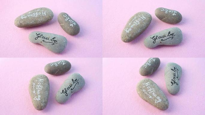 旋转粉红色背景上的三块石头，上面写着爱，相信和希望的德语单词
