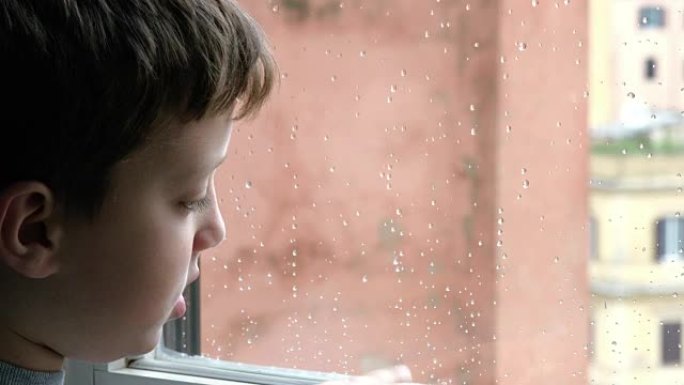 悲伤的孩子在雨中独自站在窗前