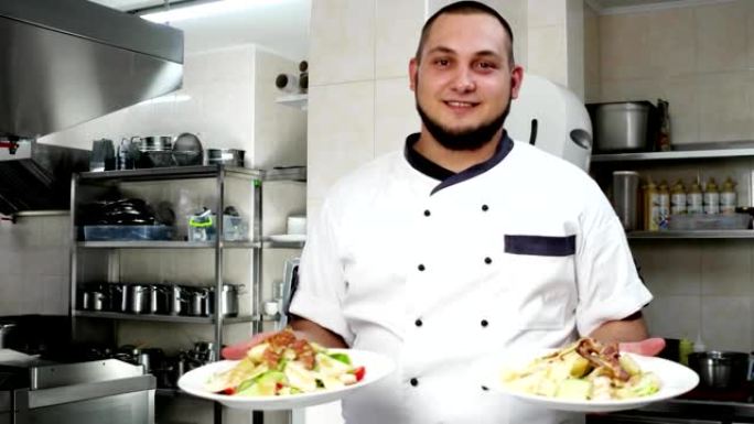 厨师的肖像，厨师拿着沙拉的菜肴，现成的饭菜表演，看着相机，微笑着厨师在专业厨房