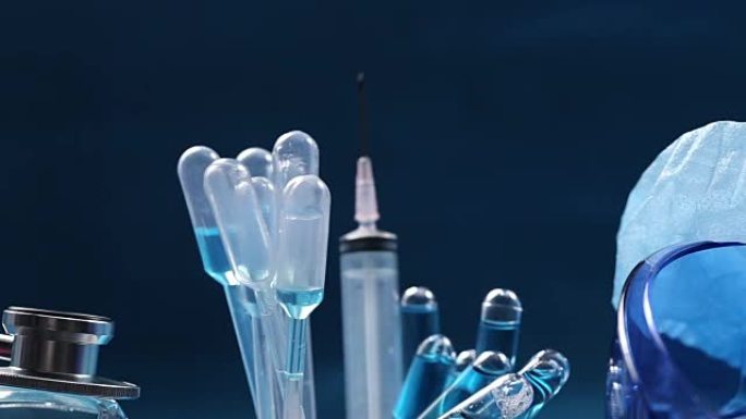 玻璃管测试实验室中的蓝色液体，滴管，注射器，模糊头盔，听诊器和护目镜，在设备上旋转的管