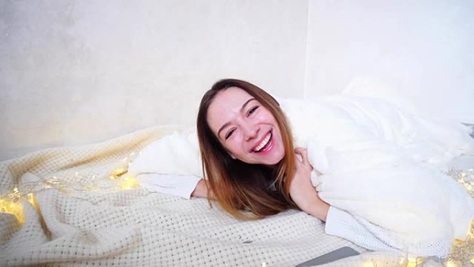迷人开朗的女孩笑着傻笑，躺在花环旁边明亮的房间里铺着毯子的地板上
