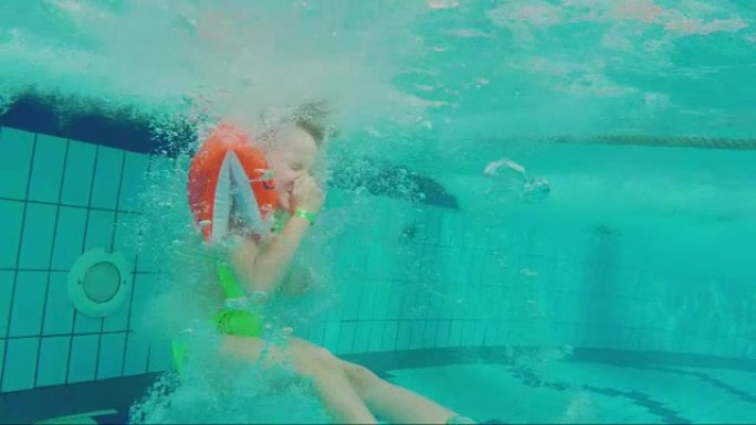 一个6岁的女孩用水滑梯掉入水中，闭上鼻子出现。水上公园娱乐，水下视频
