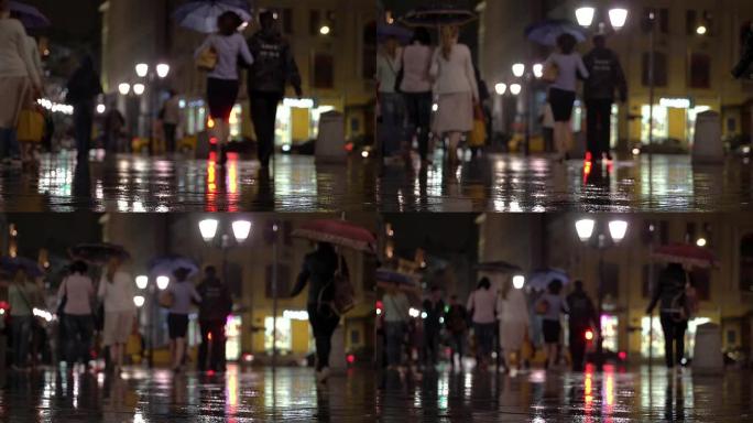 抽象背景夜雨在城市的自然黑暗色调。雨滴落在路灯照亮的五颜六色的沥青上。在行人人群中，两个朋友在雨伞下