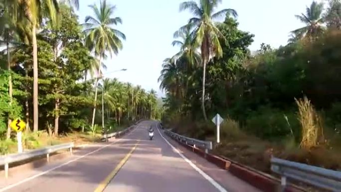 骑摩托车的人在岛上丛林中的道路上骑行的鸟瞰图