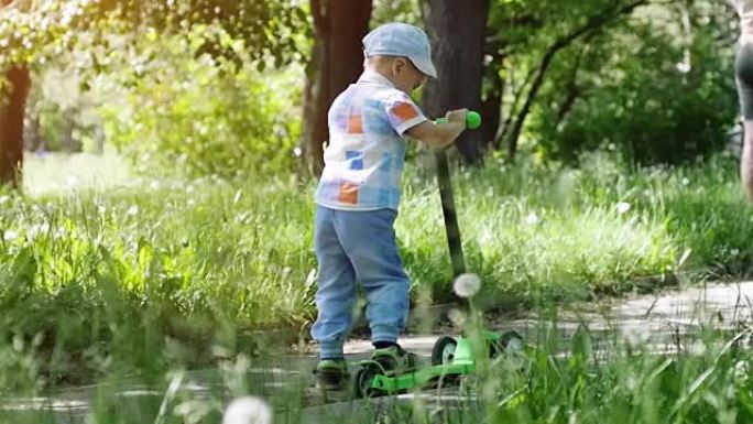 可爱的小男孩戴着帽子骑迷你踏板车，在阳光明媚的夏日慢动作在公园踢踏板车。1920x1080