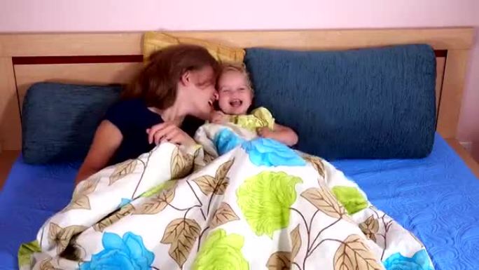 笑着的母亲和蹒跚学步的女孩在床上玩耍