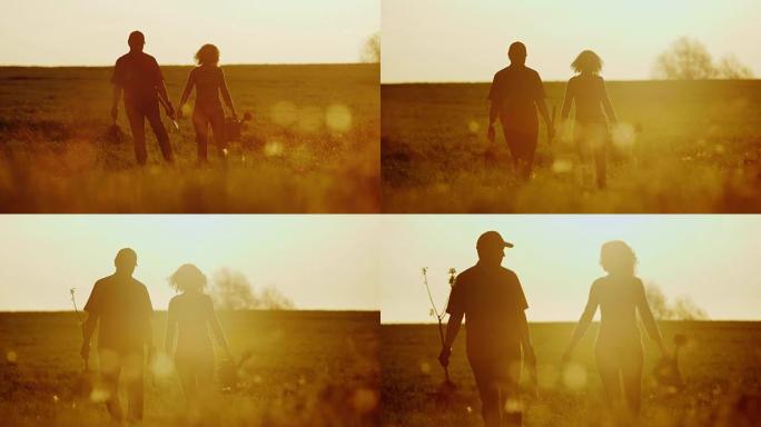 农民-日落时一男一女走过田野。携带树苗，喷壶和铲子。概念-在花园里工作，志愿服务，新生活