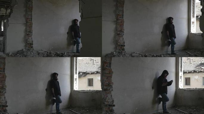 蒙面沮丧的年轻人坐在一栋废弃的建筑物中