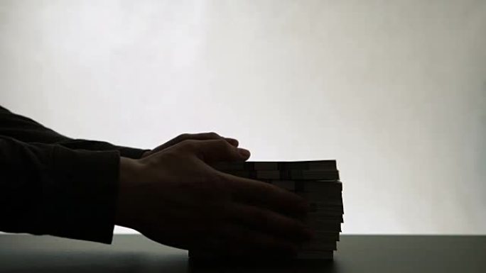 人手的剪影放在桌上一叠纸币上