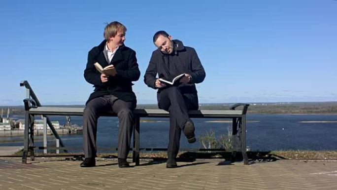两个男人坐在户外的长凳上拿着书