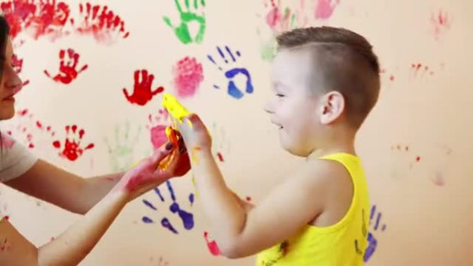 快乐的母亲和她可爱的男孩在一起玩得开心，把五颜六色的手印留在墙上。年轻幸福的家庭。母子概念