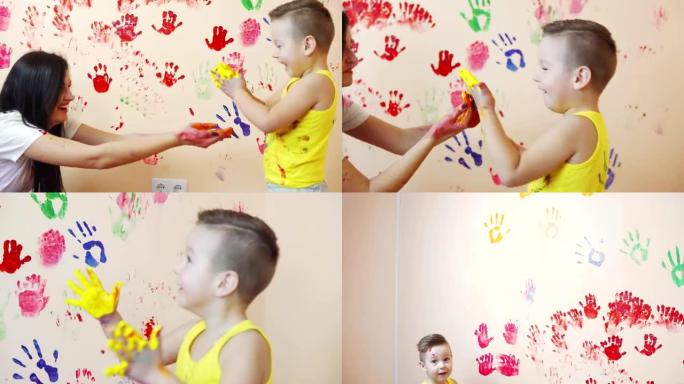 快乐的母亲和她可爱的男孩在一起玩得开心，把五颜六色的手印留在墙上。年轻幸福的家庭。母子概念