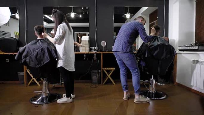 女发型师和男发型师的后视图，与坐在理发店里披着剪斗篷的客户一起工作。年轻女子和英俊男子使用客户的理发