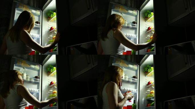 女人晚上打开冰箱。夜间饥饿。饮食。暴食