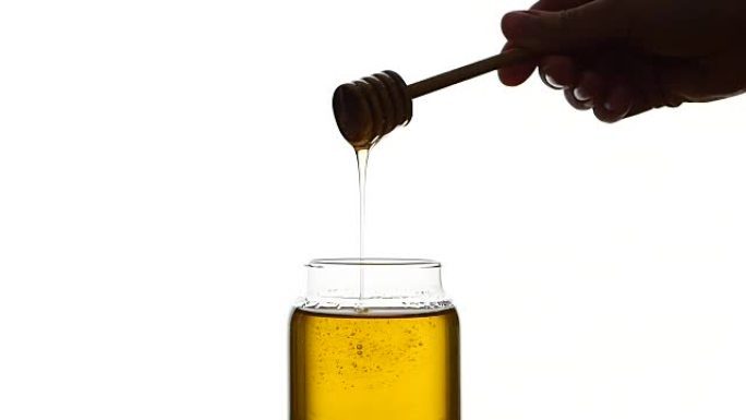 用木勺玻璃罐蜂蜜，捡起来，孤立在白色上，慢动作
