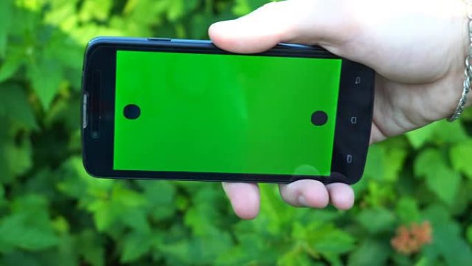 男性手持智能手机的特写镜头，带有绿屏预键效果。背景中的自然