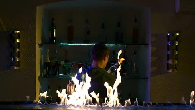专业调酒师用两个玻璃杯，摇床和瓶子站在吧台后面，抓住肘部，呕吐，放火表演，慢动作来制作酷而惊人的技巧