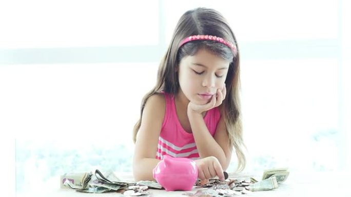 严肃的小女孩把硬币和钞票放进她的存钱罐。