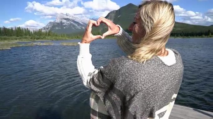 年轻女子在山湖风景上制作心形手指框架