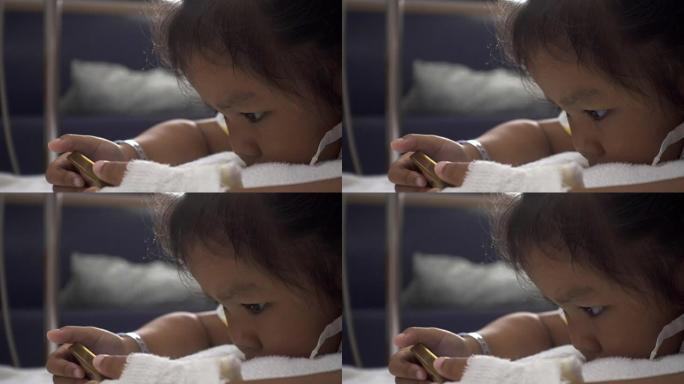 婴儿女儿在病床医院使用智能手机的特写镜头。年轻患者的放松时间。在治疗室实时拍摄。