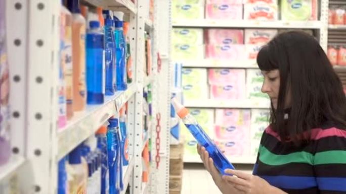 年轻女子在超市的家庭护理部门选择家用洗涤剂。货架上的各种各样