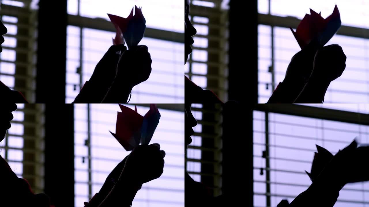 一个女孩举起她在窗户上做的折纸花，剪影