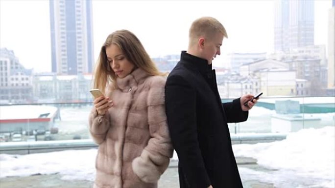 情侣在城市户外使用手机笑得开心。穿着毛皮大衣的女人