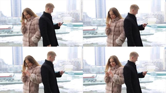 情侣在城市户外使用手机笑得开心。穿着毛皮大衣的女人