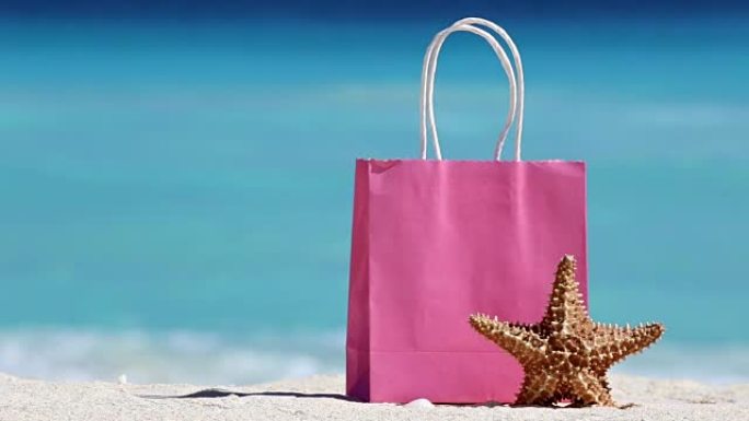 粉色购物袋和海星在沙滩上抵御绿松石加勒比海海水