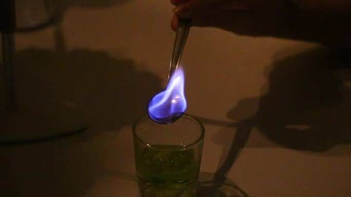 一个人准备一杯苦艾酒。糖，用浓饮料润湿，在茶匙中燃烧。