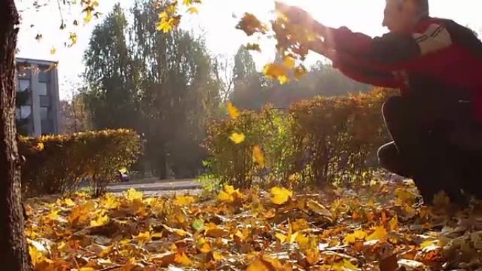 一个男人从秋天公园的树枝上扔黄色的叶子
