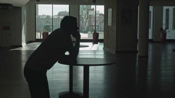 一个男人站在桌子旁的房间大厅里打电话的剪影