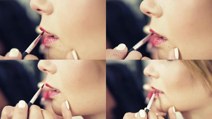 化妆师用口红刷画一个美丽女孩的嘴唇。带口红的模特。嘴唇上的粉红色唇膏。时髦的唇膏。慢动作镜头