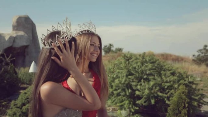 两名年轻女子留着长发，头上挂着昂贵的皇冠，站在花园里微笑着