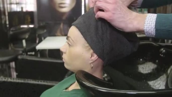 专业美发师将金发女孩的头发用水放入美容院的毛巾中。头发护理