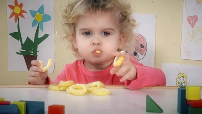 饥饿的孩子在他房间的桌子旁吃玉米薯片