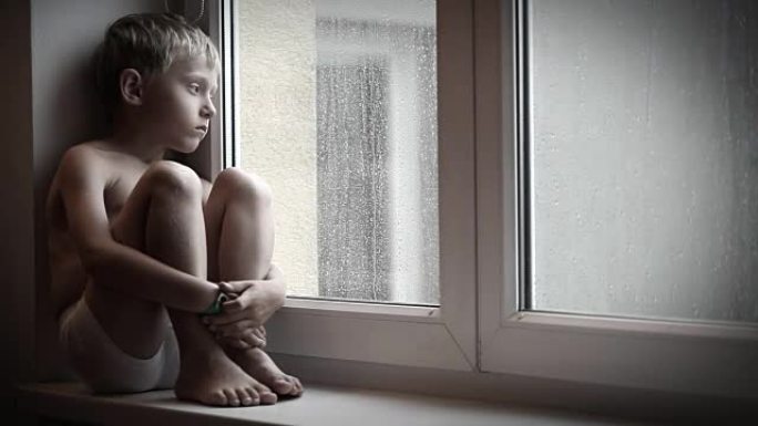 喜怒无常的小男孩坐在窗台上，看着雨滴从窗玻璃上掉下来