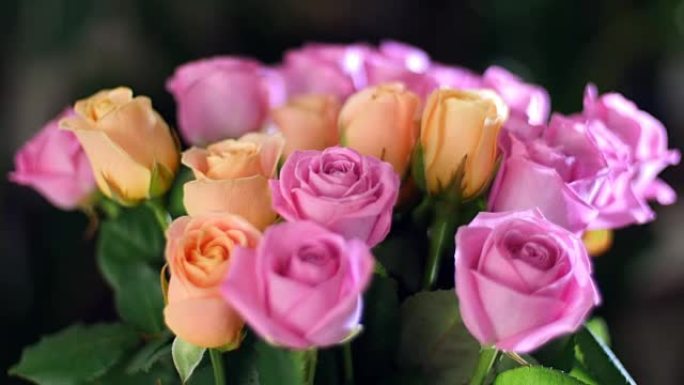 特写镜头，花束在光线中，旋转，花卉组成由粉红色和橙色玫瑰水色组成。背景中有很多绿色植物。神圣之美