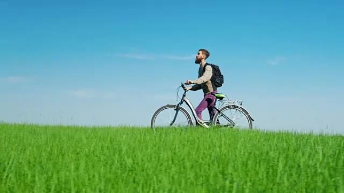 生态旅游-一个人在明亮的蓝天下驾驶自行车穿过绿色的草地。田园诗般的风景，环保的地方