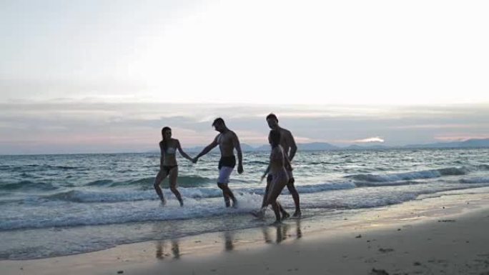 两对幸福的夫妻在日落时牵手在沙滩上散步，年轻人游客在暑假中交流