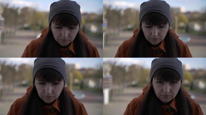 一个戴着灰色帽子的黑发女孩站在街上，她的头悲伤地下沉，抬起头若有所思，悲伤地凝视着。特写
