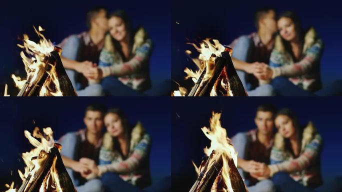 浪漫的情侣在燃烧的火中轻声交谈。火上的锋利，一对年轻夫妇被模糊了