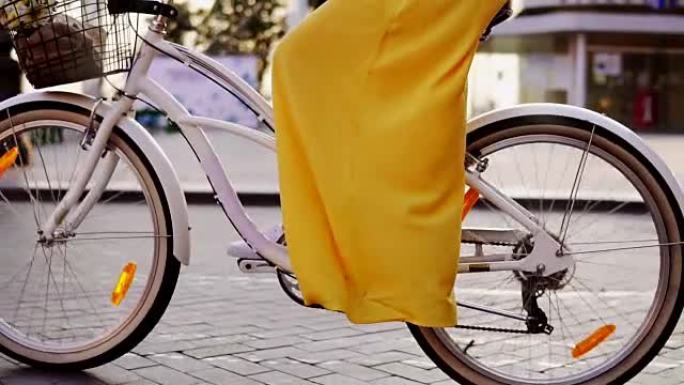 白色城市自行车车轮旋转的特写视图。带铃铛、篮子和鲜花的城市自行车。一早骑城市自行车的面目全非的女人。