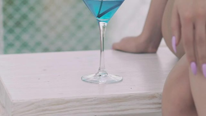 靠近裸露女人的腿的蓝色鸡尾酒杯。慢慢地