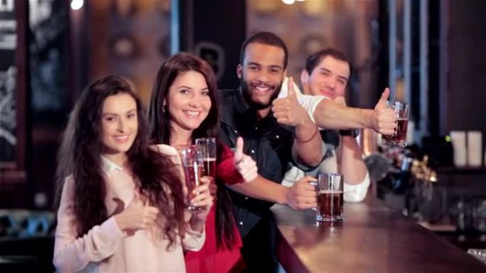 一群女孩和男孩在酒吧里，带着啤酒微笑，露出拇指