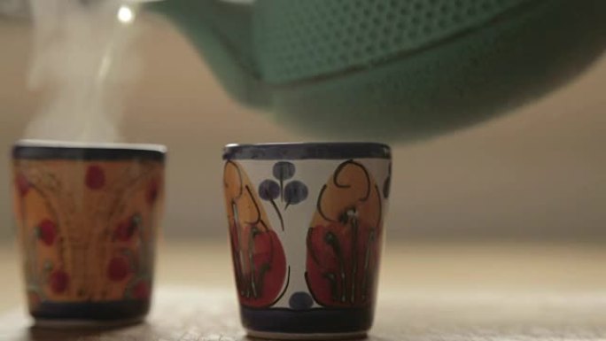 一个茶箱将热茶倒入两个陶瓷彩色杯子中
