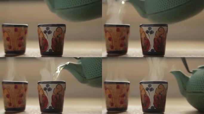 一个茶箱将热茶倒入两个陶瓷彩色杯子中
