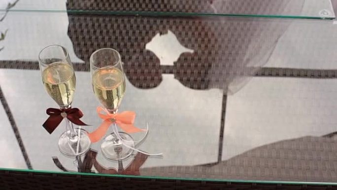 桌子上有两杯彩带的香槟。婚礼夫妇在玻璃上的倒影。